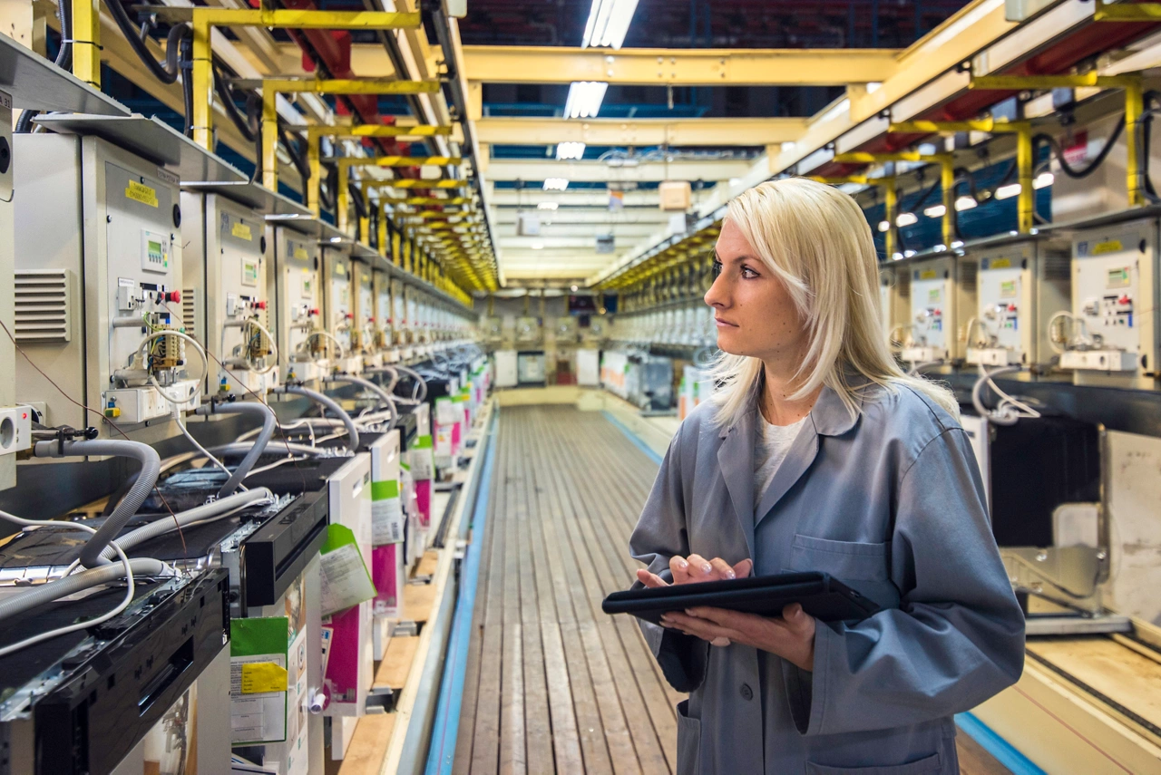 Female factory worker entering data into a digital tablet while checking the machine in appliance manufacturing factory.