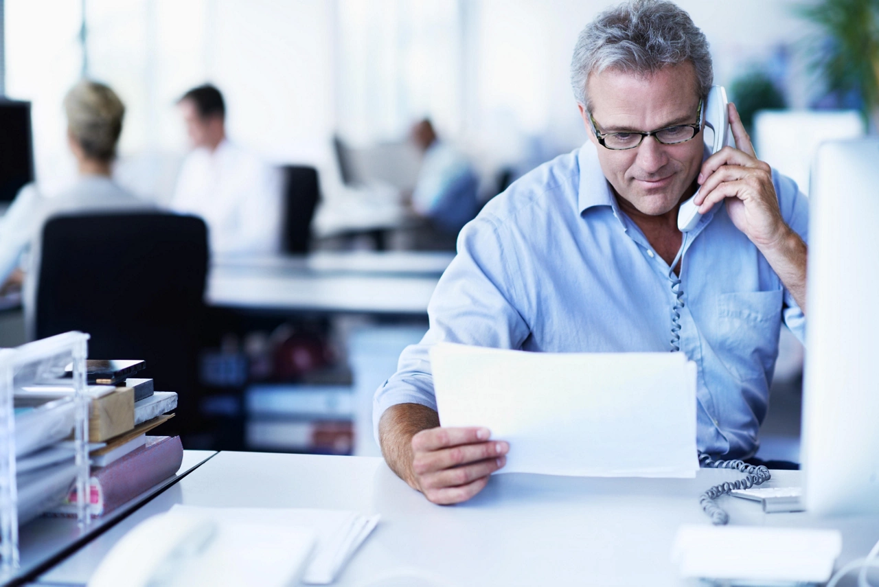 Shot of a mature businessman talking on a phone and reading a document while sitting at his desk in an office